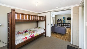 A bunk bed with a floral bedspread in a room with a wooden floor, a gray sofa, and a bookshelf in the adjacent living area. - Blueshack - Walking distance to foreshore (Guilderton)