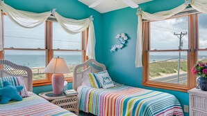 Una habitación con dos camas, ventilador de techo y ventanas amplias con vistas al océano.