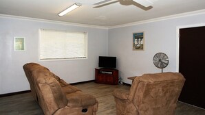 A living room with a ceiling fan, a television, and two brown leather chairs.
