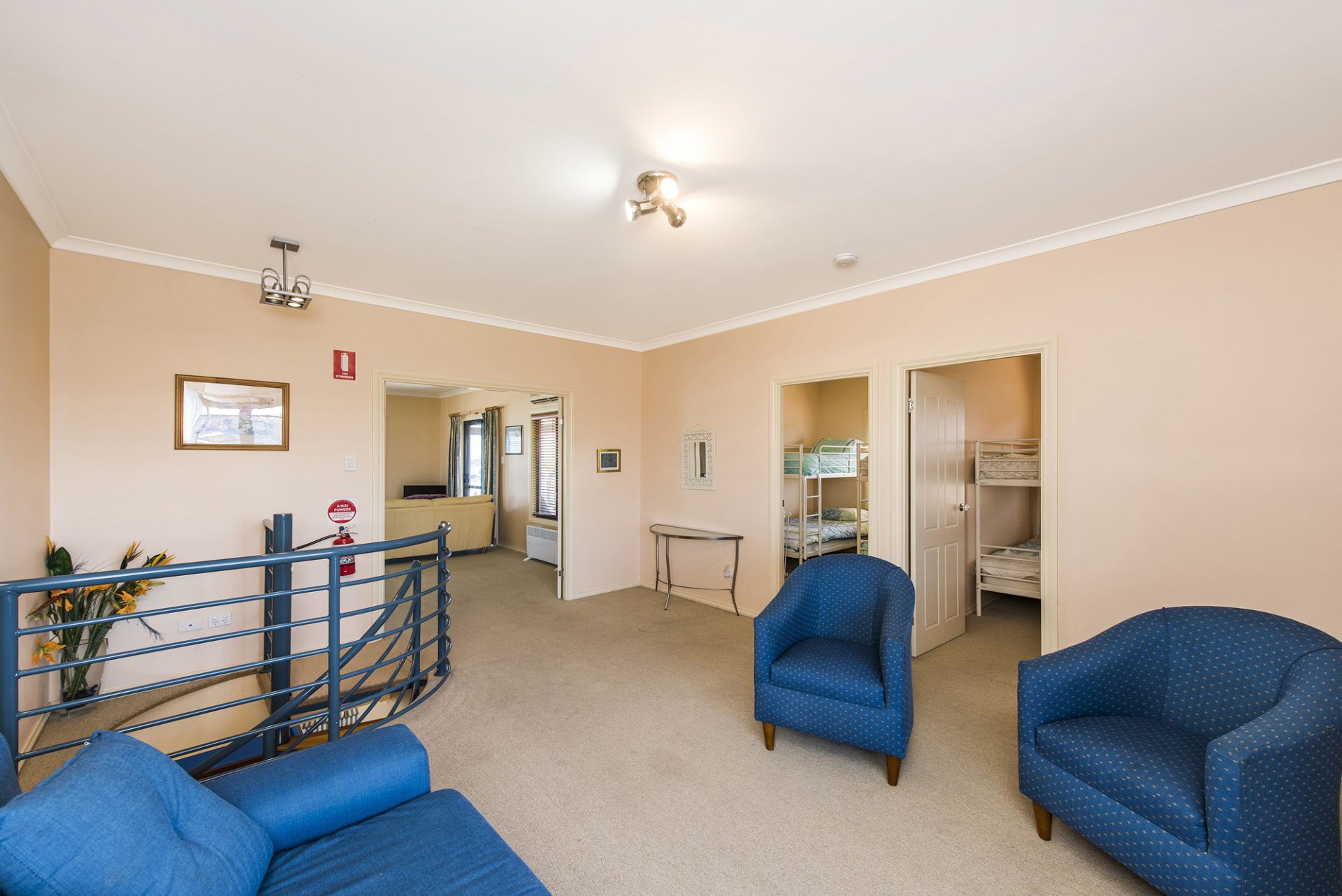 A hotel room with a bunk bed, a blue armchair, a small table, and a staircase leading to another room.