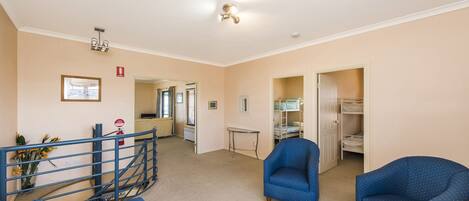A hotel room with a bunk bed, a blue armchair, a small table, and a staircase leading to another room.