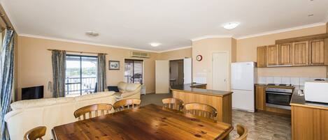 Un'ampia zona giorno con tavolo da pranzo in legno, divano beige e cucina con mobili e elettrodomestici in legno.