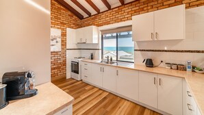 A kitchen with white cabinets, a brick wall, wooden beams, a window, and a coffee maker. - Ocean View Retreat - Best Views in town (Guilderton)