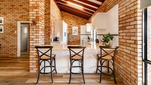 A kitchen with exposed brick walls, wooden beams, and a central island with bar stools. - Ocean View Retreat - Best Views in town (Guilderton)