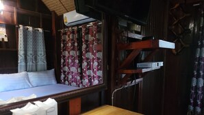 A room with a bed, a wooden table with a remote control, and a window with curtains. - Pairom Resort (Saraburi)
