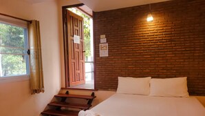 A hotel room with a wooden floor, a bed with white bedding, a wooden bench, and a brick wall. - Pairom Resort (Saraburi)