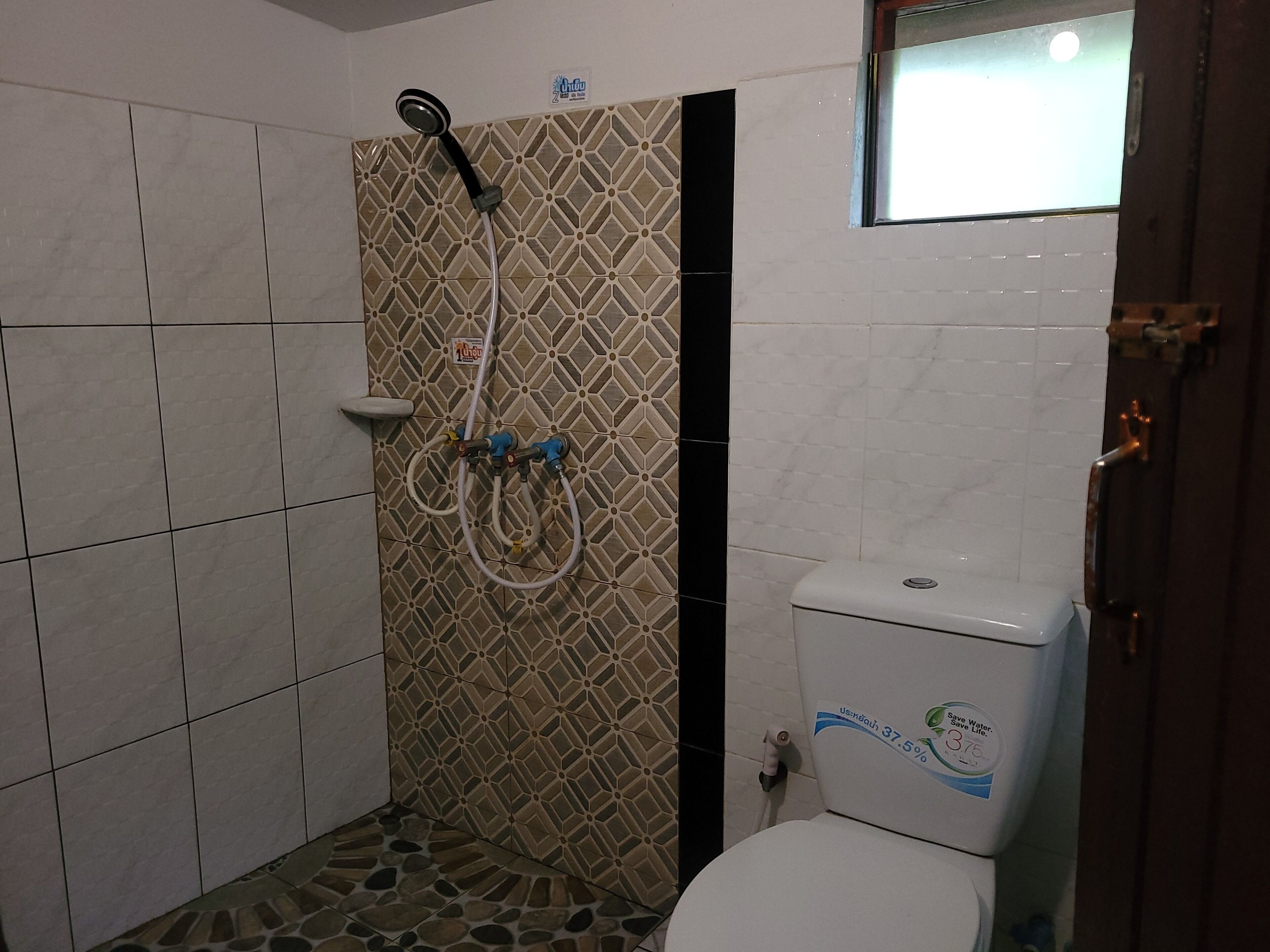 Un baño con inodoro, ducha y pared de azulejos con diseño geométrico.