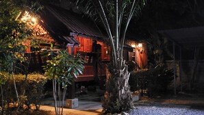 A traditional wooden house with a thatched roof, surrounded by lush greenery and a gravel pathway. - Pairom Resort (Saraburi)