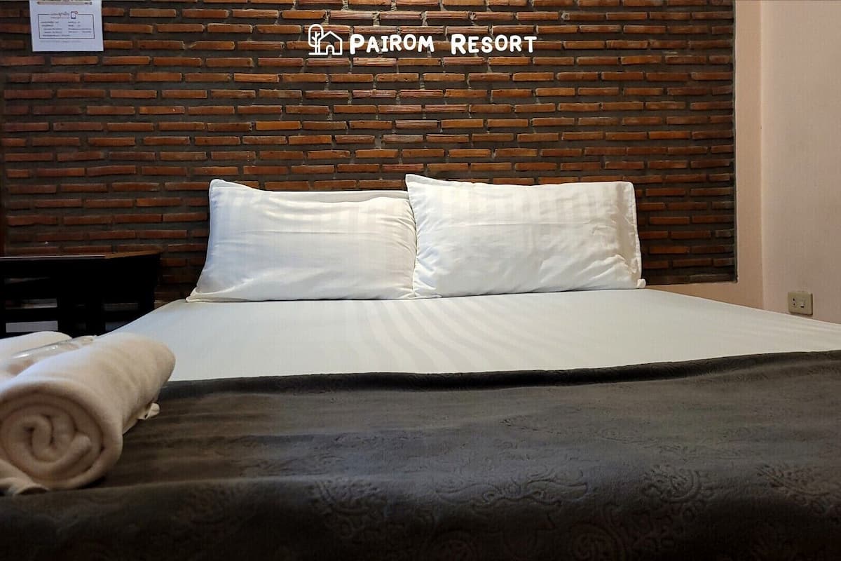 Een hotelkamer met een hoofdeinde met een bakstenen patroon, een net opgemaakt bed met witte lakens, en een opgerolde handdoek op het bed.