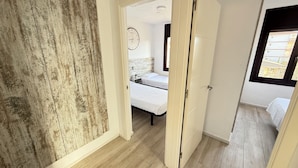 Een smalle gang met aan de ene kant een houten wand en aan de andere kant een slaapkamer met een bed en een klok.