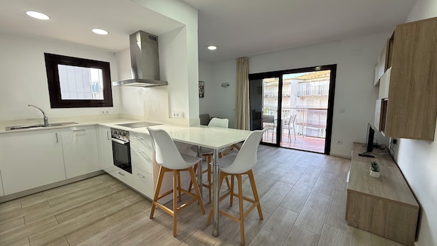 Een moderne keuken met witte kasten, een roestvrijstalen afzuigkap en een eethoek met twee witte stoelen.