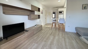 Een moderne woonkamer met een flatscreen-televisie, houten vloeren, een zithoek met twee stoelen en een grijze bank.