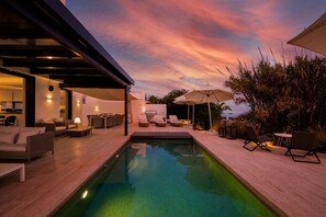 Relax by the serene pool surrounded by a deck with lounge chairs and a table.