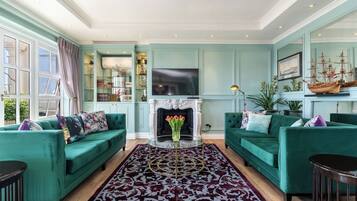 A spacious living room with teal walls, two green sofas, a fireplace, and a large TV.
