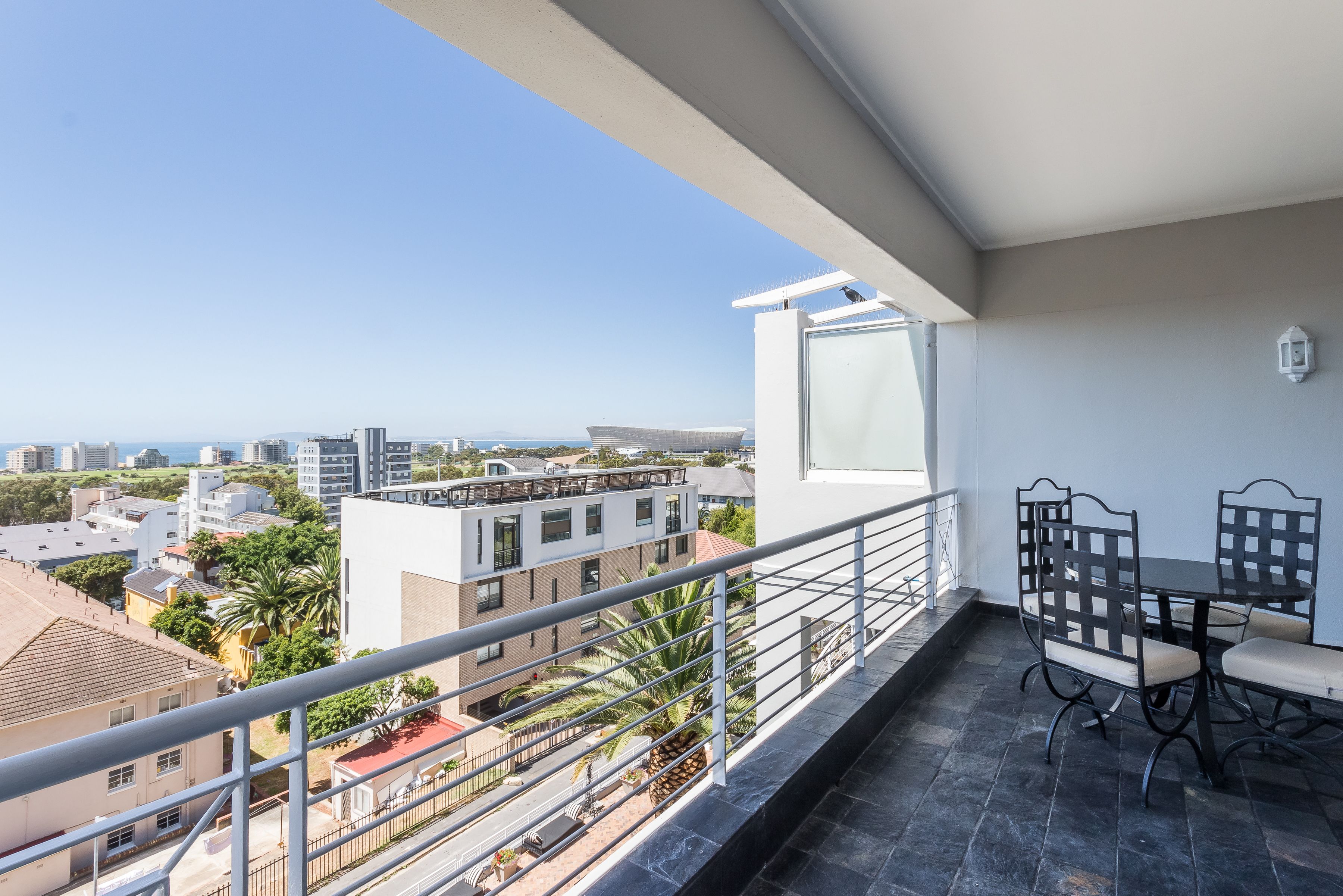 Varanda com mesa e cadeiras, vista para um horizonte urbano com edifícios e palmeiras.