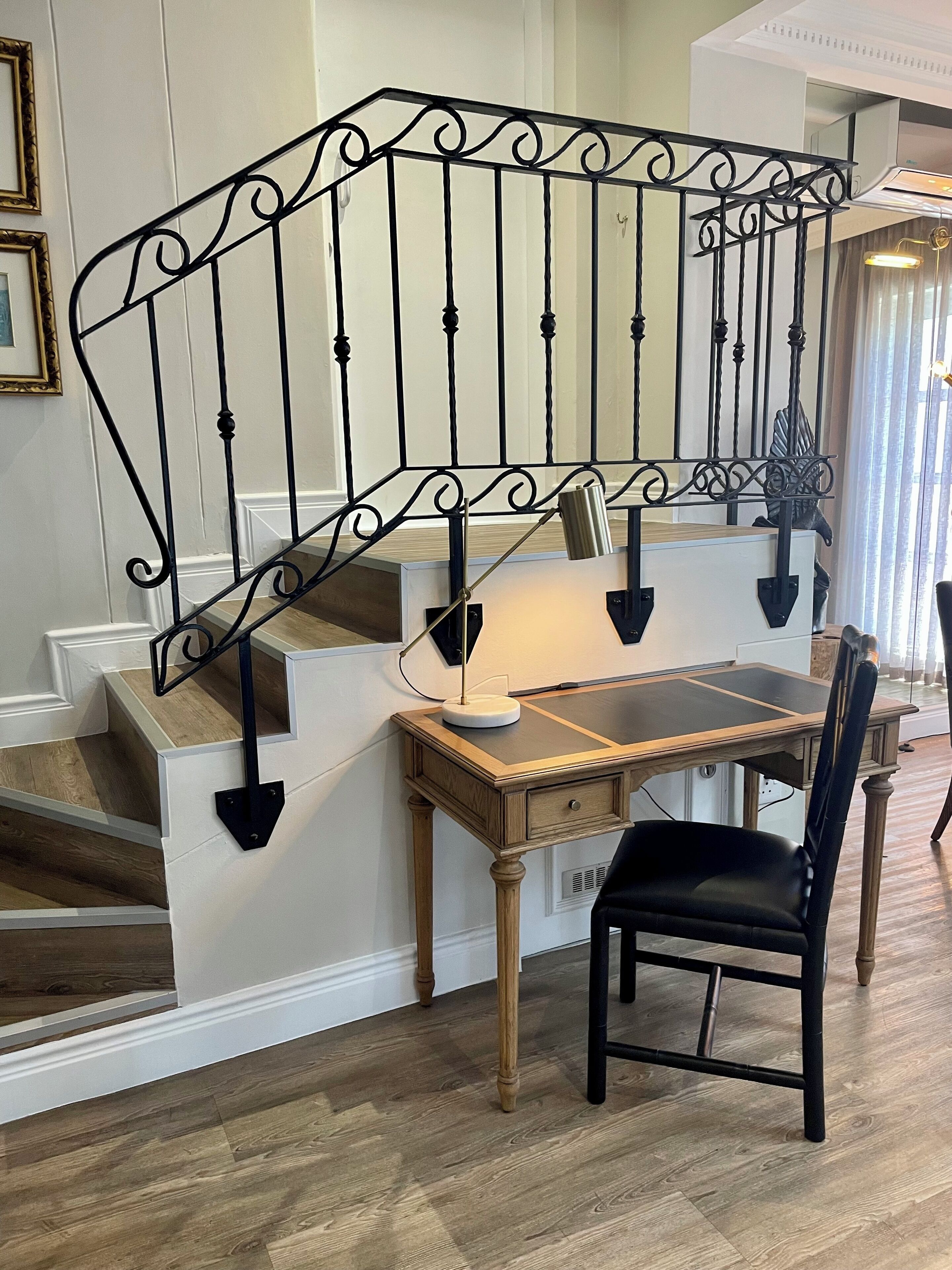 A staircase with a black metal railing, a wooden desk with a lamp, and a black chair.
