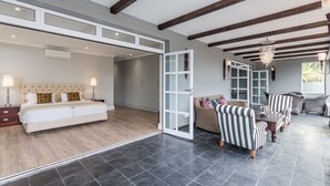 Une chambre spacieuse avec un grand lit, un coin salon avec des fauteuils à rayures et une vue sur l’extérieur.