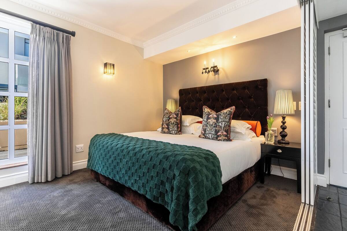 Une chambre d’hôtel avec un grand lit, une table de chevet, une lampe et une vue sur l’extérieur par une fenêtre.