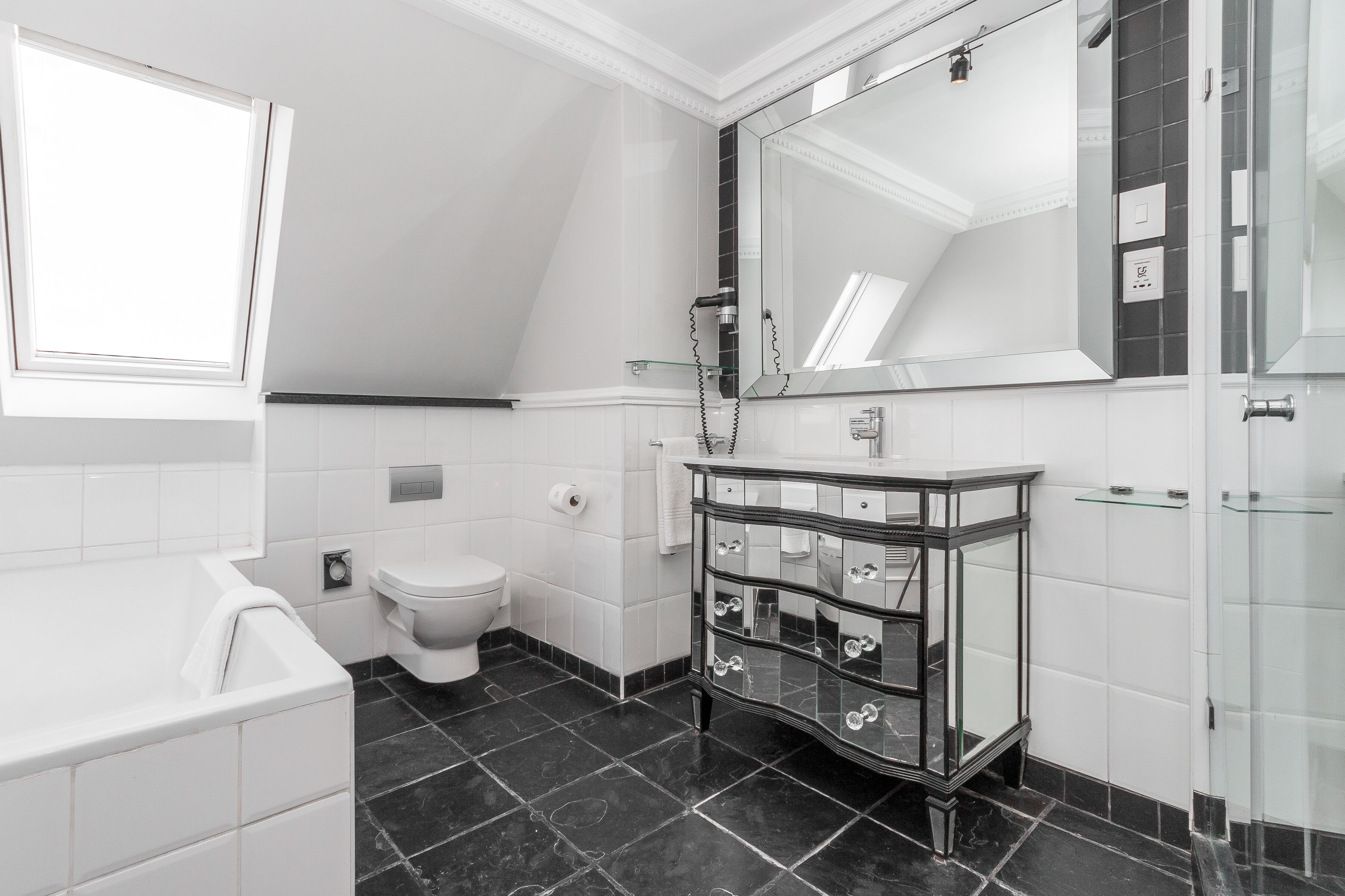 Une salle de bain moderne avec une baignoire blanche, un meuble-lavabo avec un encadrement en verre, un grand miroir et des toilettes.
