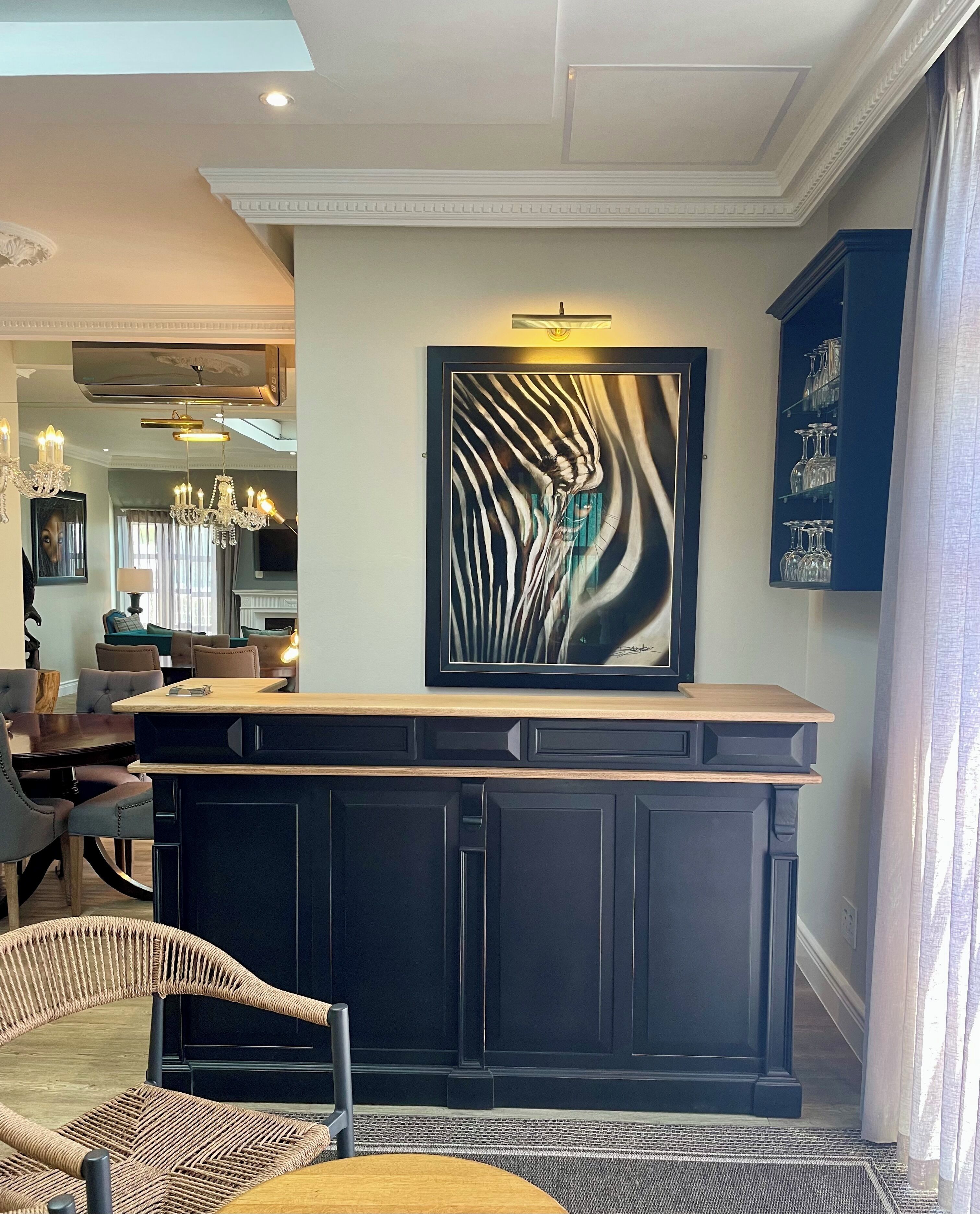 Un salon moderne avec un bar en bois foncé, une grande peinture abstraite et un coin repas avec des chaises en osier.