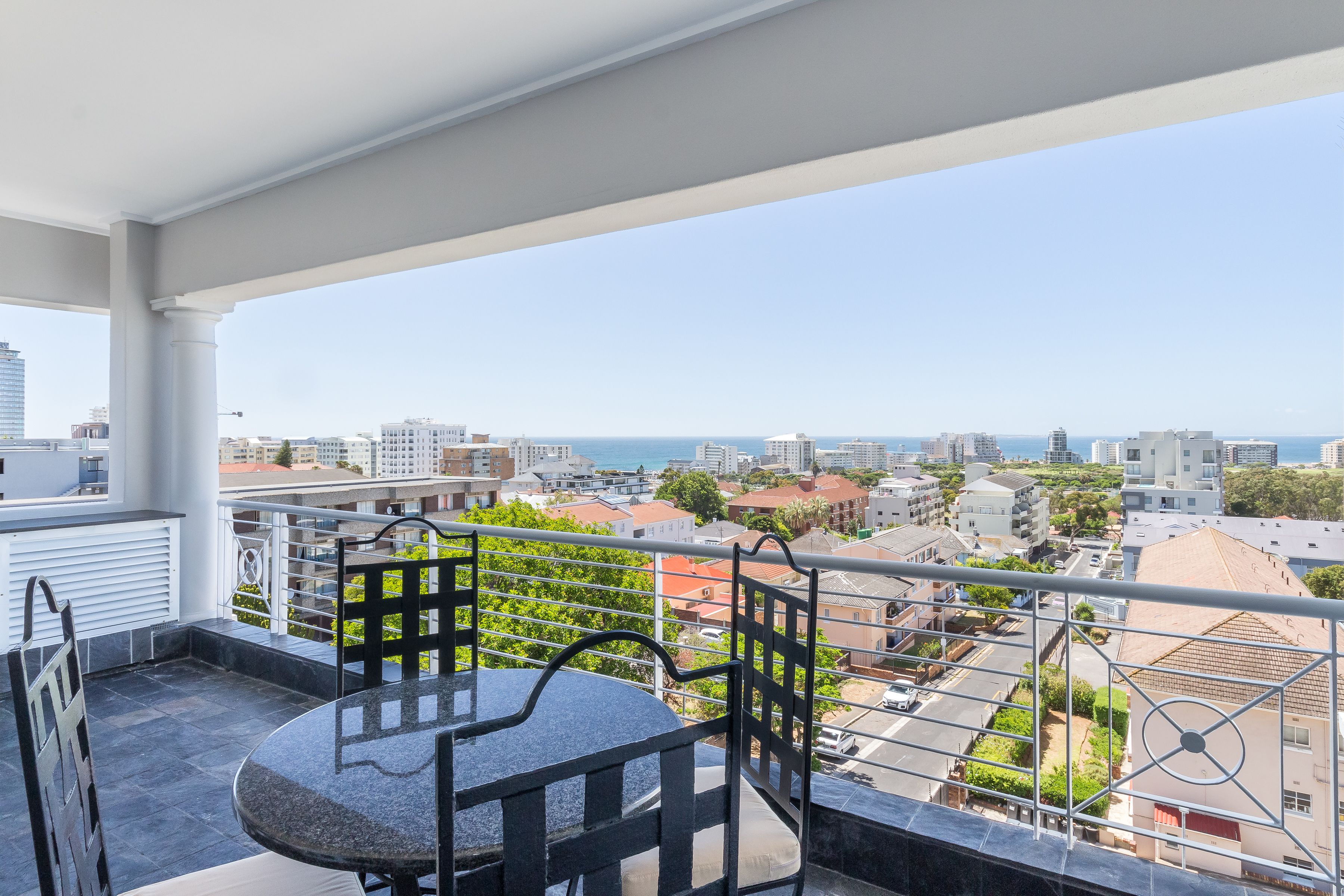 A balcony with a table and chairs, offering a view of the city and the sea.