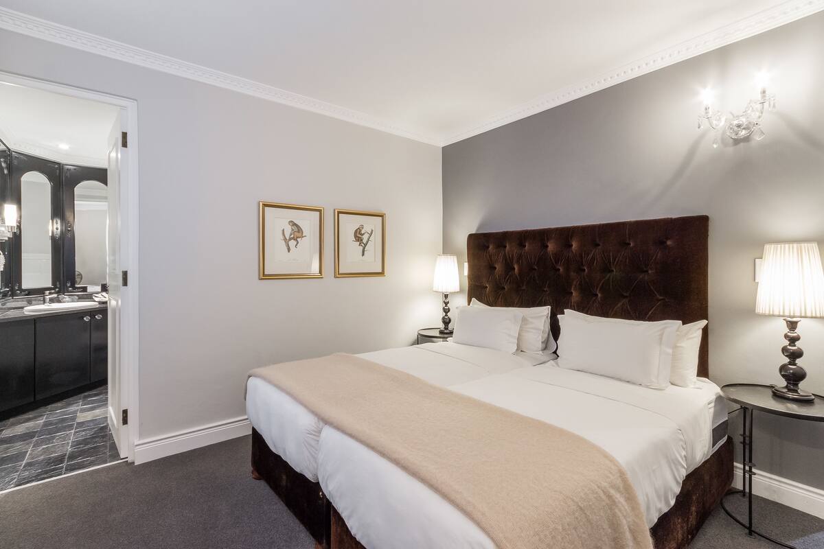 Une chambre d’hôtel avec un grand lit, une table de chevet avec une lampe, un miroir et deux tableaux encadrés au mur.