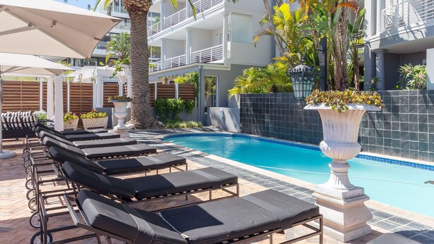 Un espace aménagé au bord de la piscine, avec des chaises longues, un palmier et une piscine carrelée.