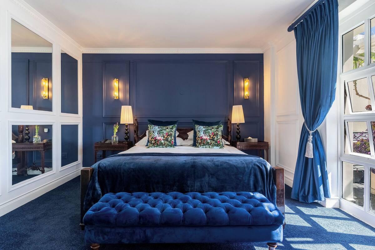 Une chambre à coucher avec un grand lit, deux tables de chevet et une fenêtre avec des rideaux.
