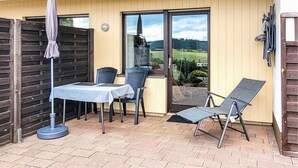 An outdoor patio with a table and chairs, a folding chair, a window with a view of a green landscape, and a wooden fence. - 1 bedroom cozy apartment in Medebach-Düdinghausen (Medebach-Düdinghausen)