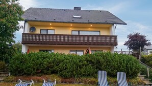 A two-story house with a balcony, surrounded by a well-maintained garden and three striped lounge chairs. - 1 bedroom cozy apartment in Medebach-Düdinghausen (Medebach-Düdinghausen)