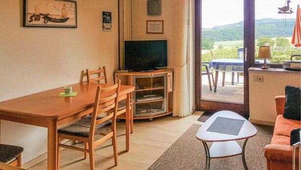A dining area with a wooden table and chairs, a television on a stand, and a view of a garden through a glass door. - 1 bedroom cozy apartment in Medebach-Düdinghausen (Medebach-Düdinghausen)