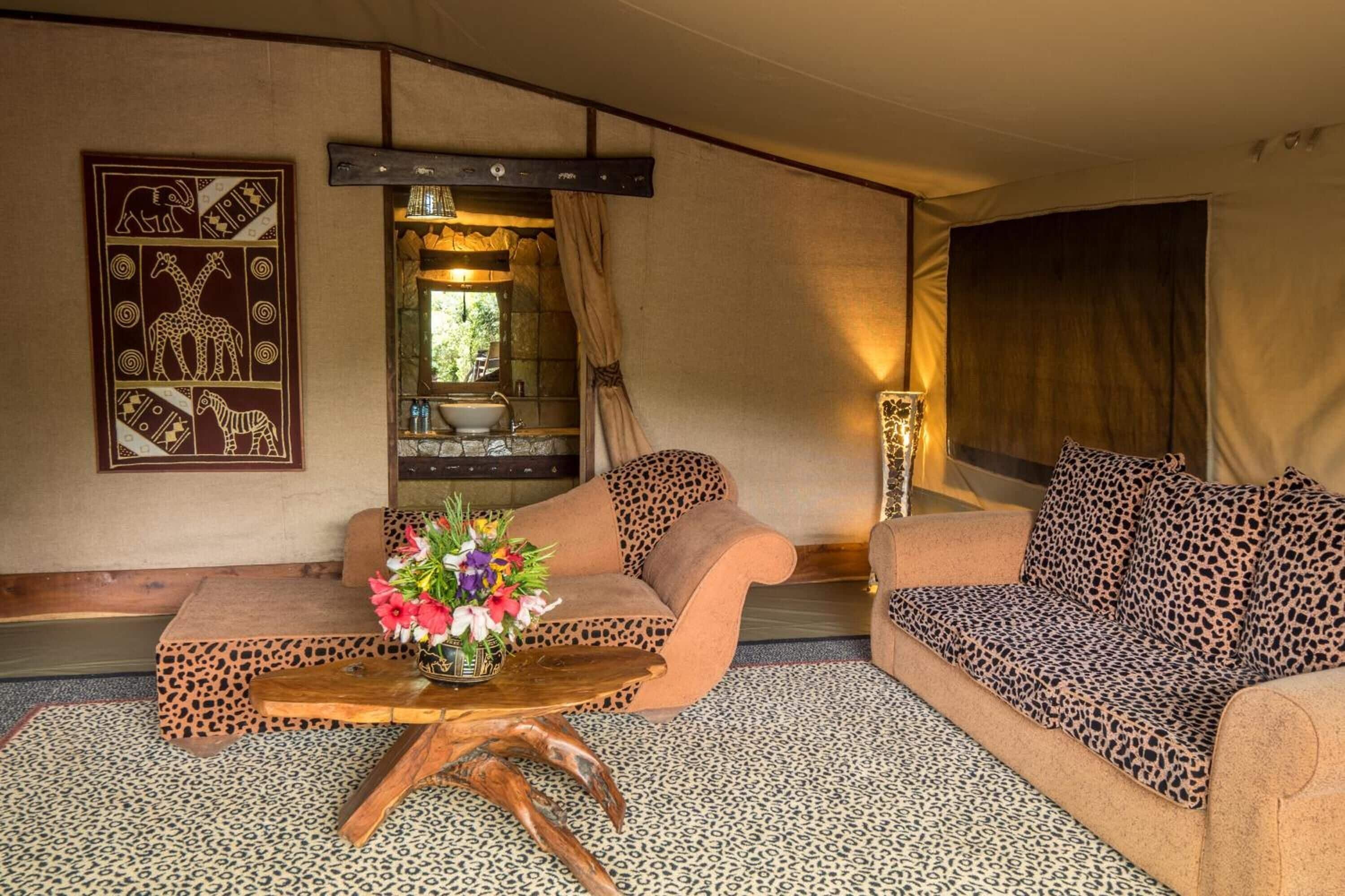 Una habitación con dos sofás tapizados con estampado de leopardo, una mesa de centro de madera con un jarrón de flores y una pared decorada con arte tribal.