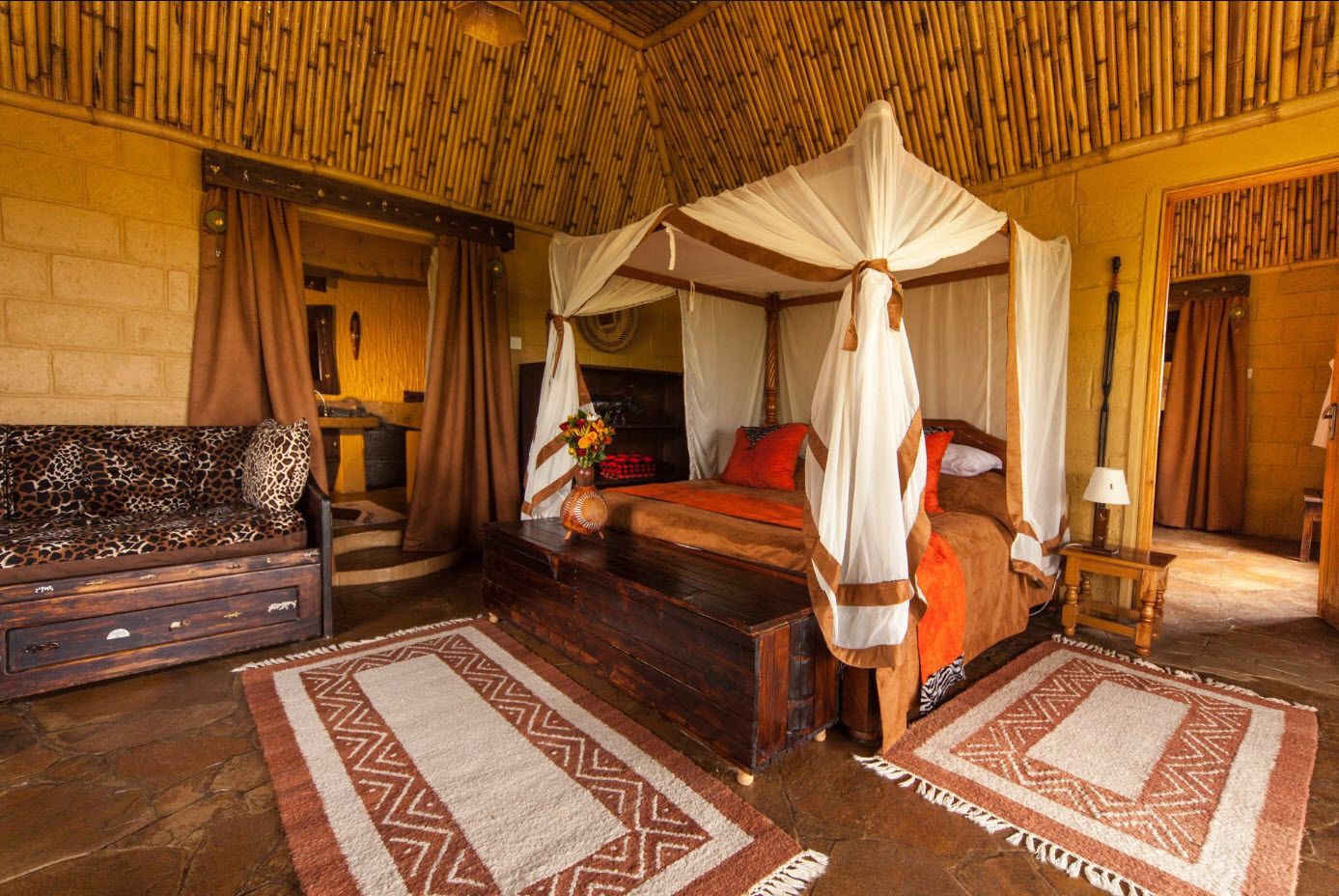 A room with a four-poster bed, a sofa, a wooden chest, and a nightstand.