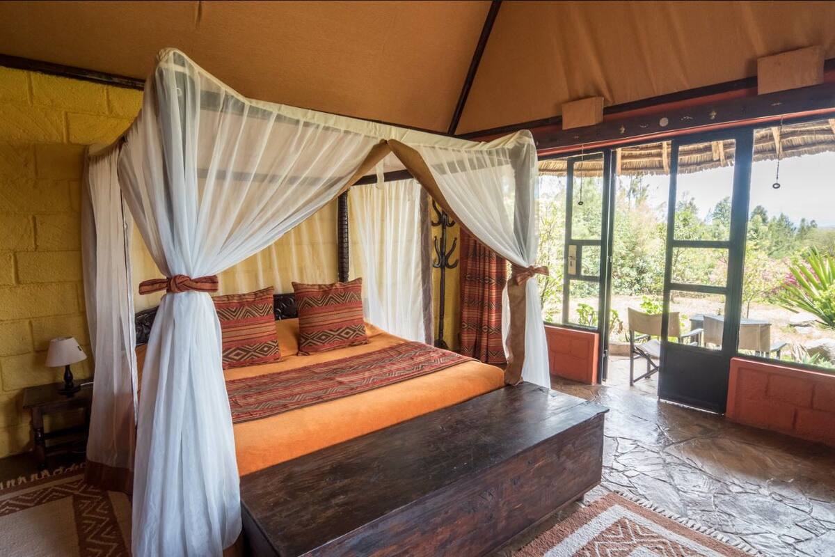 Una cama con dosel, una mesita de noche con lámpara, y vistas al exterior a través de amplias ventanas.