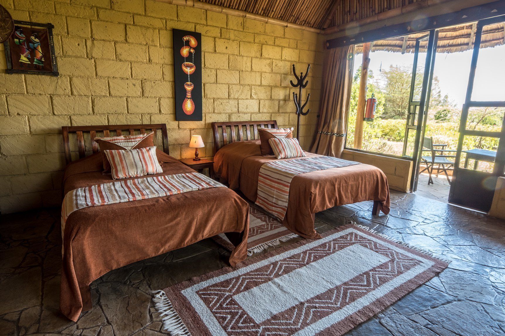 A room with two beds, a stone floor, a large window, and a wall with a decorative item.