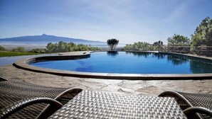 A circular infinity pool with a clear view of mountains in the background, surrounded by a stone deck and wicker lounge chairs. - Rhino Watch safari Lodge (Nyahururu)