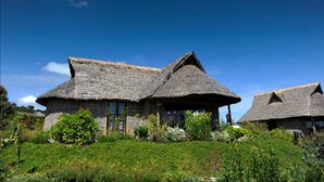 A traditional thatched-roof house with a stone foundation, surrounded by a lush garden with various plants and flowers. - Rhino Watch safari Lodge (Nyahururu)