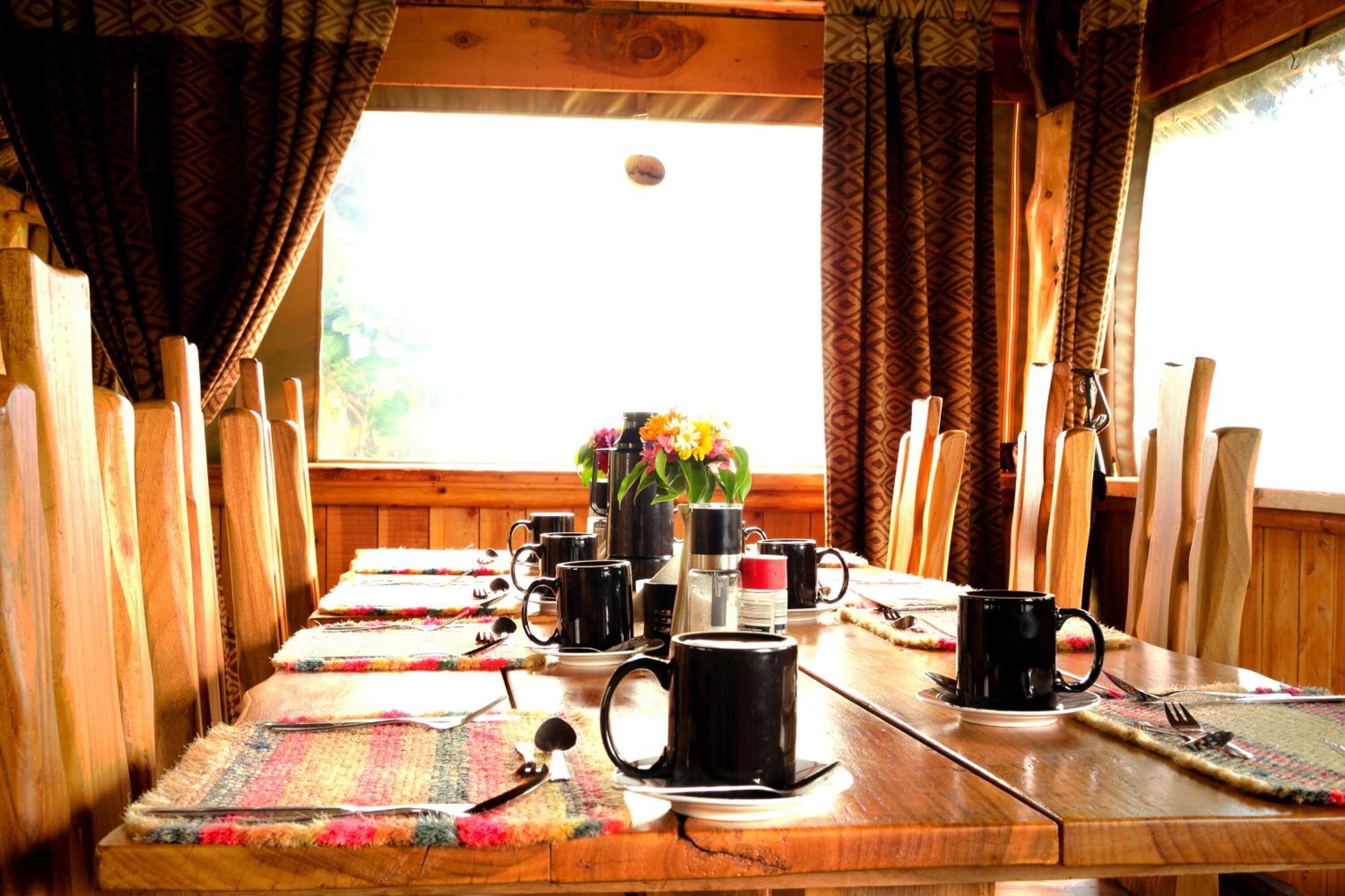A wooden dining table with black mugs, a flower vase, and a wooden chair.