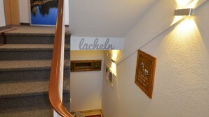 Un escalier avec une rampe en bois, des marches recouvertes de moquette, une enseigne fixée au mur portant l’inscription « Lachel » et une citation encadrée.