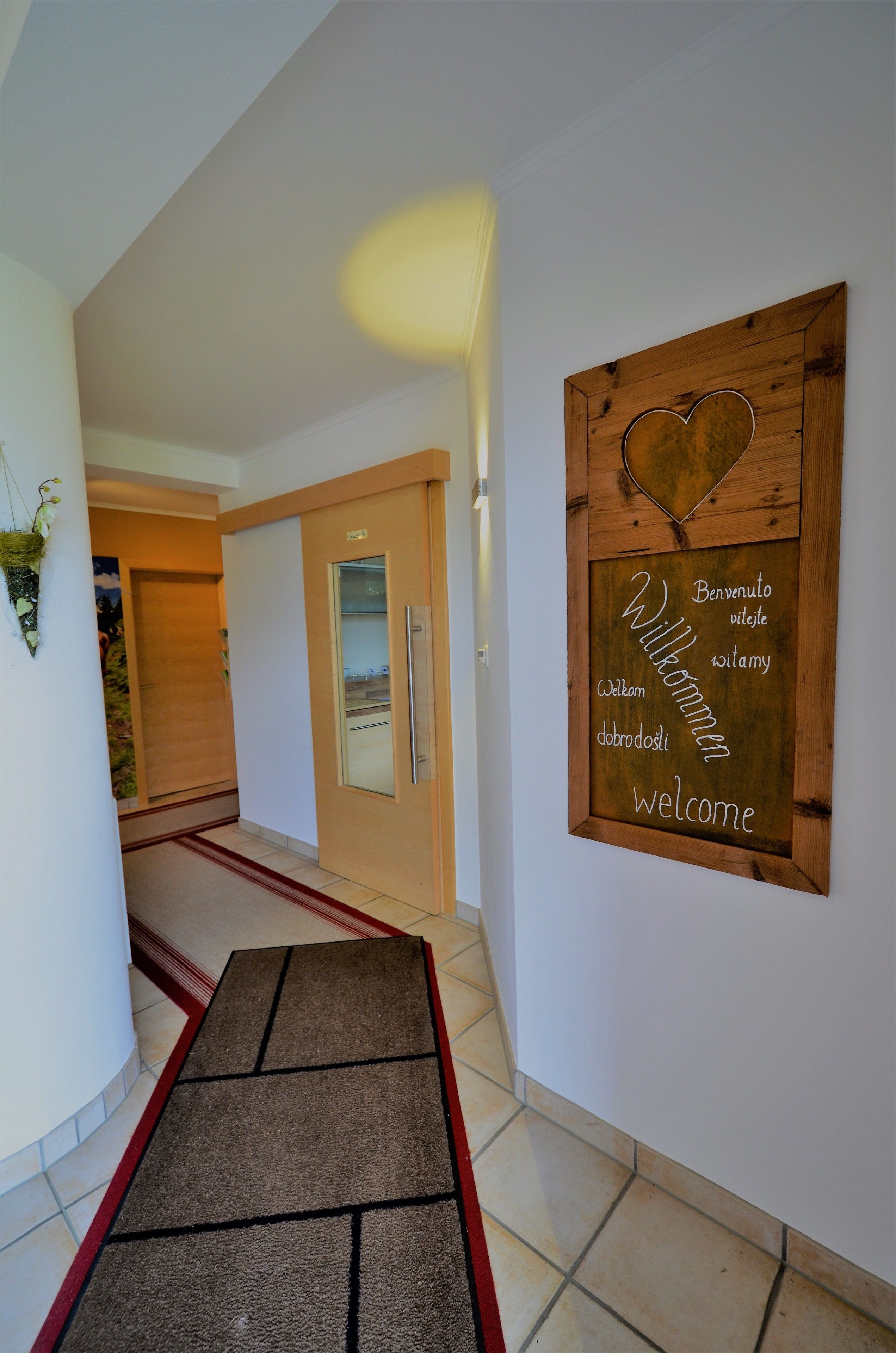 Un pasillo con un letrero de madera que dice 'Bienvenido', una puerta y una alfombra roja que conduce a una habitación.