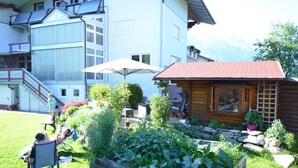 Un bâtiment à deux étages, avec une structure en bois rappelant une cabane, situé au premier plan, un jardin bien entretenu et un escalier menant à l’étage supérieur.