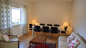 Un salon comprenant un canapé, deux fauteuils, une table basse en bois, une table à manger avec des chaises, et une fenêtre avec des rideaux.