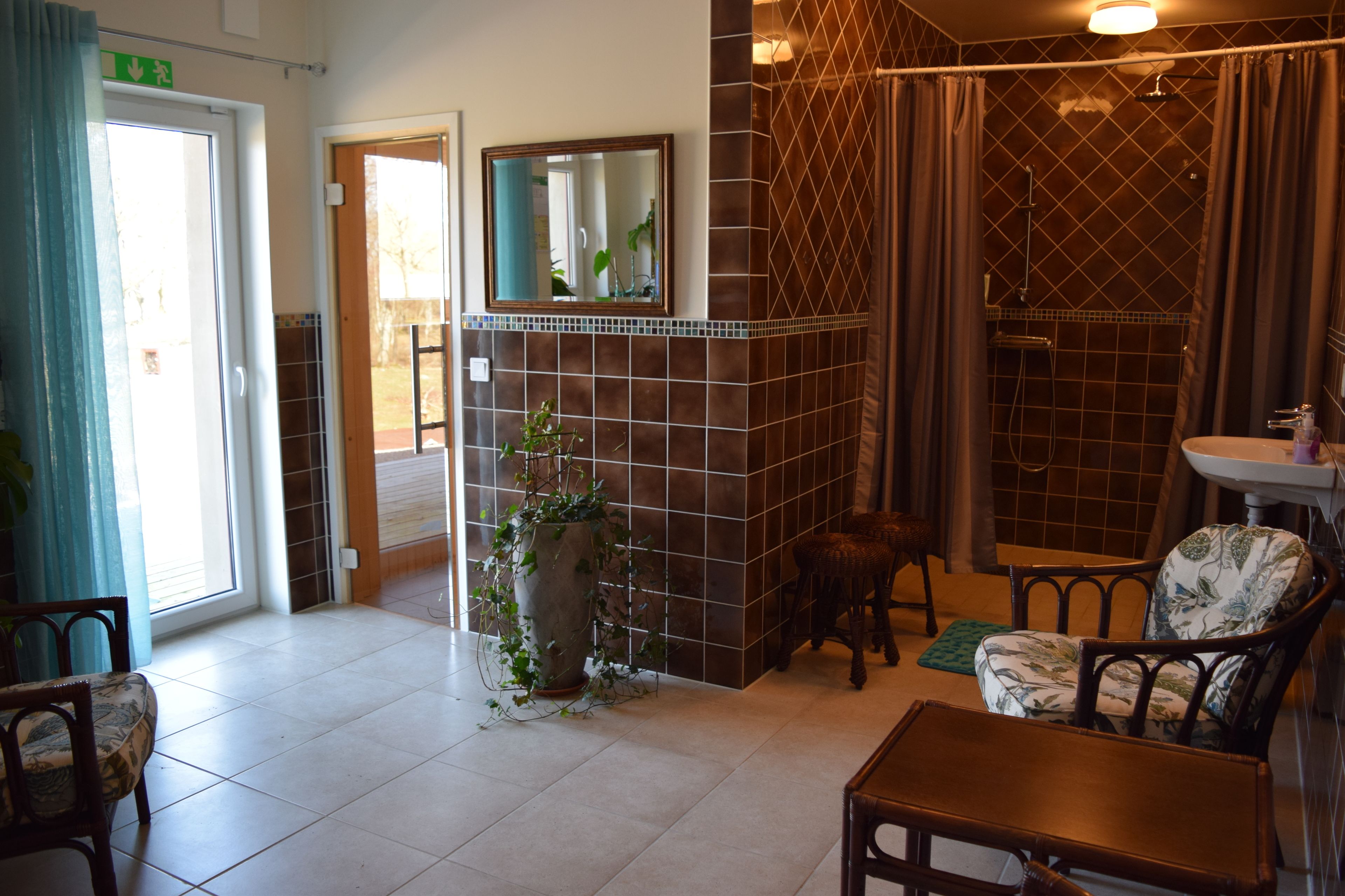 A bathroom with a shower, a sink, and a mirror. There is a potted plant and a chair in the room.