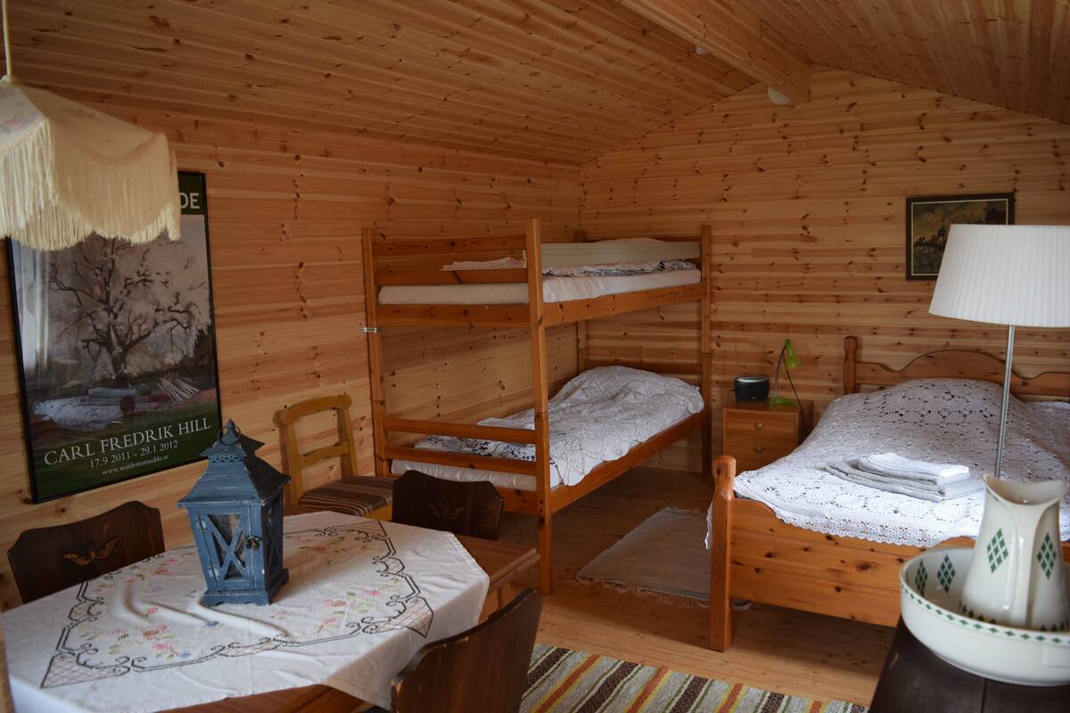 A wooden cabin with bunk beds, a table with a tablecloth, a lamp, and a poster on the wall.