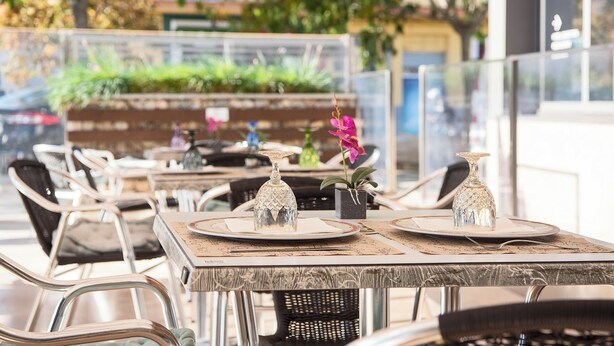 An outdoor dining area with tables set for two, featuring metal chairs and a glass table. - Hotel Palau de girona (Sant Julia de Ramis)