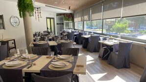 A restaurant with multiple tables set for dining, large windows with a view of the street, and a clock on the wall. - Hotel Palau de girona (Sant Julia de Ramis)