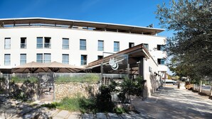 A modern building with a flat roof, multiple windows, and a covered outdoor seating area with umbrellas. - Hotel Palau de girona (Sant Julia de Ramis)