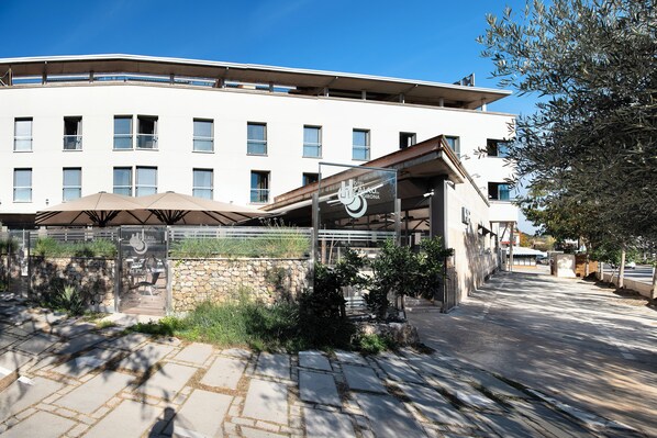 A modern building with a flat roof, multiple windows, and a covered outdoor seating area with umbrellas. - Hotel Palau de girona (Sant Julia de Ramis)