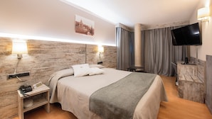 A modern hotel room with a large bed, a flat-screen TV, a bedside table with a lamp, and a power outlet. - Hotel Palau de girona (Sant Julia de Ramis)