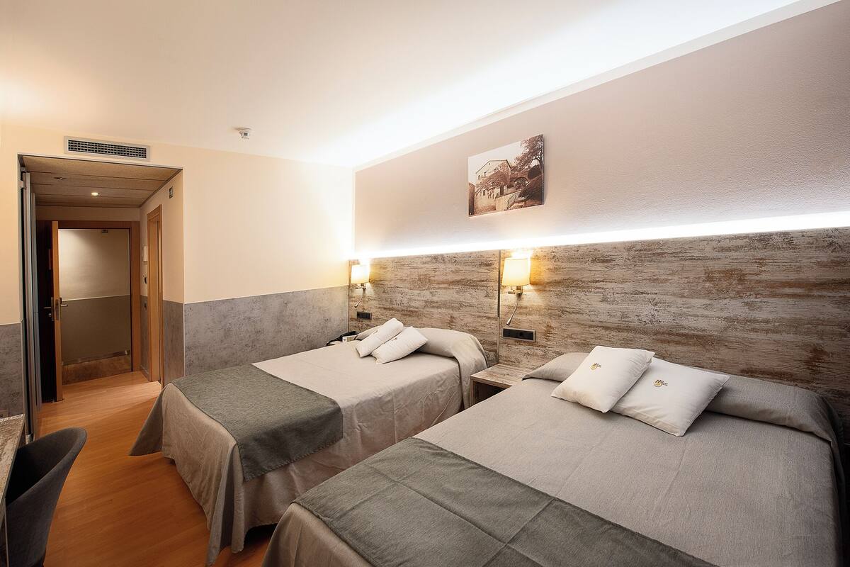 Une chambre d’hôtel avec deux lits, une tête de lit en bois, un tableau accroché au mur et une porte donnant sur une autre pièce.